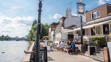 En café ved floden med udendørs siddepladser, en lygtepæl og et skilt til pubben 'The Bell & Crown'.