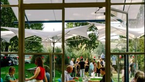 An indoor event with tables and chairs, a glass partition, and an outdoor garden visible through the glass. - The Courtyard Oasis Studio (London)