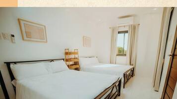 A hotel room with two beds, a wooden chair, a small table, and a window with curtains.