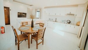 Une cuisine moderne avec des meubles blancs, un coin repas doté d’une table ronde et de chaises, et un téléviseur à écran plat fixé au mur.