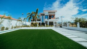 Une maison moderne à deux étages, dotée d’un grand jardin à l’avant et surplombant un ciel d’un bleu limpide.
