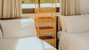 Une chambre d’hôtel avec deux lits, une fenêtre avec des rideaux, un fauteuil en osier et un appareil de climatisation.