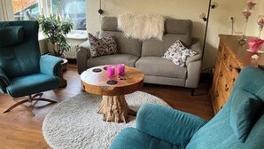 Ein gemütliches Wohnzimmer mit einem türkisfarbenen Sessel, einem grauen Sofa, einem Holztisch und einem flauschigen Teppich.