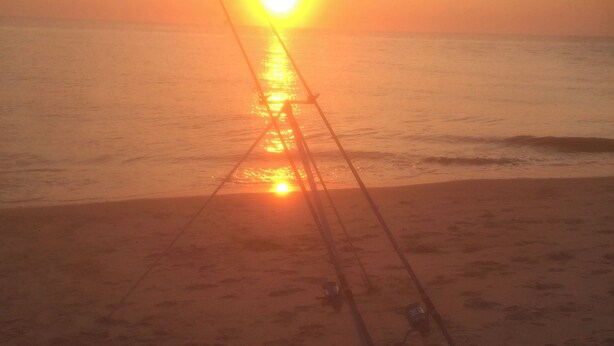 Ein Sonnenuntergang über einem Strand, Angeln mit mehreren gegenüber der Sonne ausgerichteten Ruten.