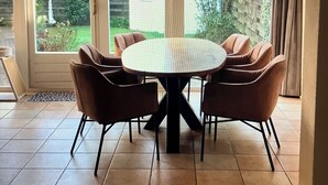 Ein Essbereich mit rundem Tisch, sechs Stühlen, großen Bogenfenstern und Blick auf einen Garten.