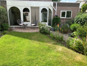 A patio with two chairs, a small table, and a garden with various plants and flowers. - Comfortable and lovely house in beautiful Bergen. (Bergen)