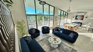 A spacious living area with large windows, a dining table, and blue sofas. - Spacious 6 & 8 bedroom Chalet Vista al Mar with AC and solar power in Aguadilla (aguadilla)