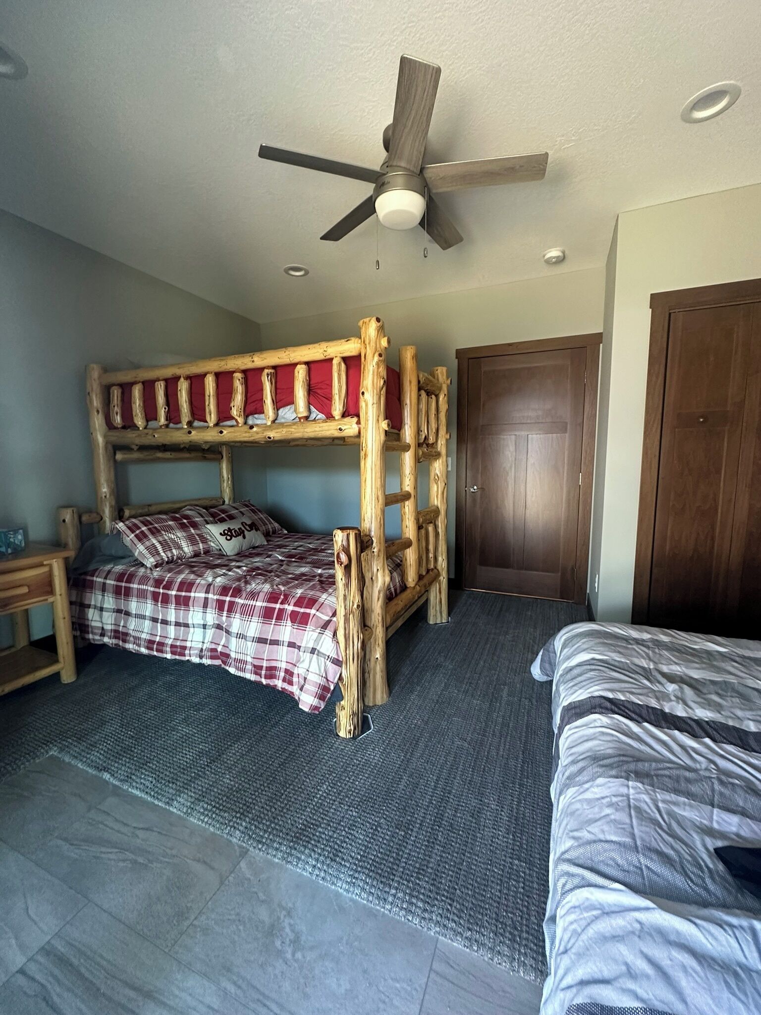 Ein Schlafraum mit Etagenbetten, Deckenventilator, Holztür und Teppichboden.