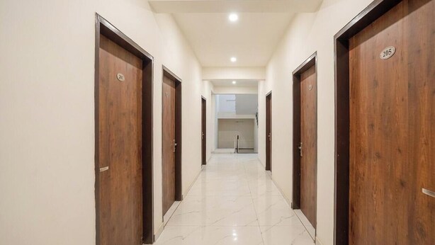 A corridor with wooden doors, each marked with a number, leading to a room with a white tiled floor and a ceiling light. - COZY COVE (Dera Bassi)