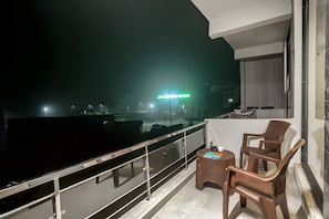 Un balcon donnant sur une vue panoramique de la ville la nuit, une petite table avec des chaises et une rambarde en verre.
