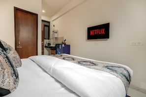 Une chambre à coucher avec un lit, un panneau Netflix fixé au mur, une porte et un bureau avec un ordinateur.