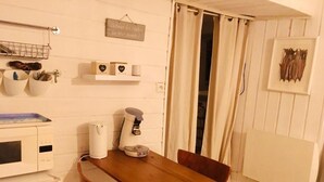A small kitchen with a wooden table, two chairs, a microwave, and a coffee maker. There is a shelf with decorative items and a sign on the wall. - Les Studios de la Côte Roz: Voyageur Solo, (Perros-Guirec)
