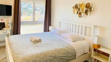 Ein ordentlich eingerichtetes Hotelzimmer mit Bett, Nachttisch, Fernseher und einem Fenster mit Vorhängen.