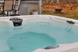 A hot tub with a clear blue water surface, surrounded by a patio area with chairs and a fire pit. - Family Alpine Retreat | Hot Tub • Sauna (Tobyhanna)