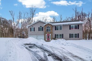 A two-story house with a stone entrance, a garage, and a driveway partially covered by snow. - Family Alpine Retreat | Hot Tub • Sauna (Tobyhanna)