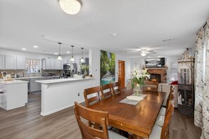 A modern kitchen with white cabinets, a central island, pendant lighting, and a dining area with a wooden table and chairs. - Family Alpine Retreat | Hot Tub • Sauna (Tobyhanna)
