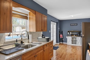 A kitchen with wooden cabinets, a sink, a coffee bar, and a view of the outdoors. - Summit Chalet at Stillwater (Pocono Summit)