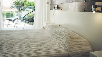 Une chambre avec un grand lit, une petite table et une chaise près d’un balcon.