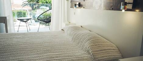 A bedroom with a large bed, a small table, and a chair near a balcony.