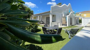 Une maison moderne à l’extérieur blanc, dotée d’un patio avec des meubles d’extérieur et d’une pelouse bien entretenue.