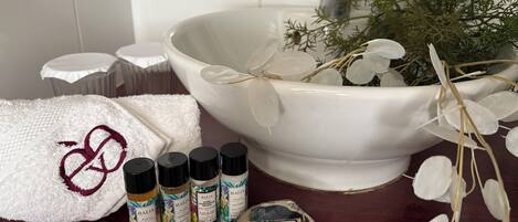 A bathroom with a large white basin, a white towel with a red logo, and several bottles of Baija hair care products.
