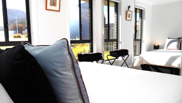 A hotel room with a bed, a chair, and a view of the outdoors through large windows. - THE QUARTERS #1 Centrally located modern 2 bed unit featuring stylish decor (East Tamworth)