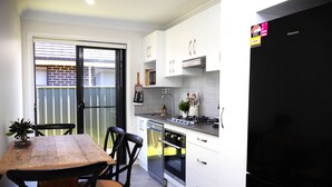 A modern kitchen with white cabinets, a black refrigerator, and a wooden dining table with chairs. - THE QUARTERS #1 Centrally located modern 2 bed unit featuring stylish decor (East Tamworth)