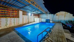 An indoor swimming pool with a wooden deck, a metal ladder, and colorful wall decorations. - Hotel Silver Leaf (Panchgani)