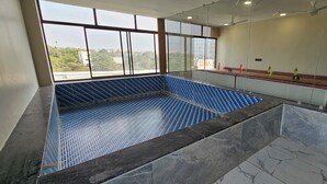 Un'ampia piscina coperta con pavimento piastrellato in blu, circondata da un muro in pietra e un'area relax con vista sulla città.