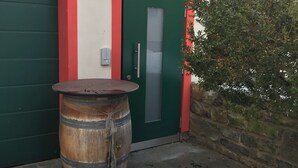 Un edificio con puerta verde y marco rojo, un barril de madera y una planta en maceta con nieve.