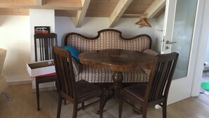 Un área de comedor con una mesa y sillas de madera, un sofá estampado y una puerta blanca con panel de vidrio esmerilado.