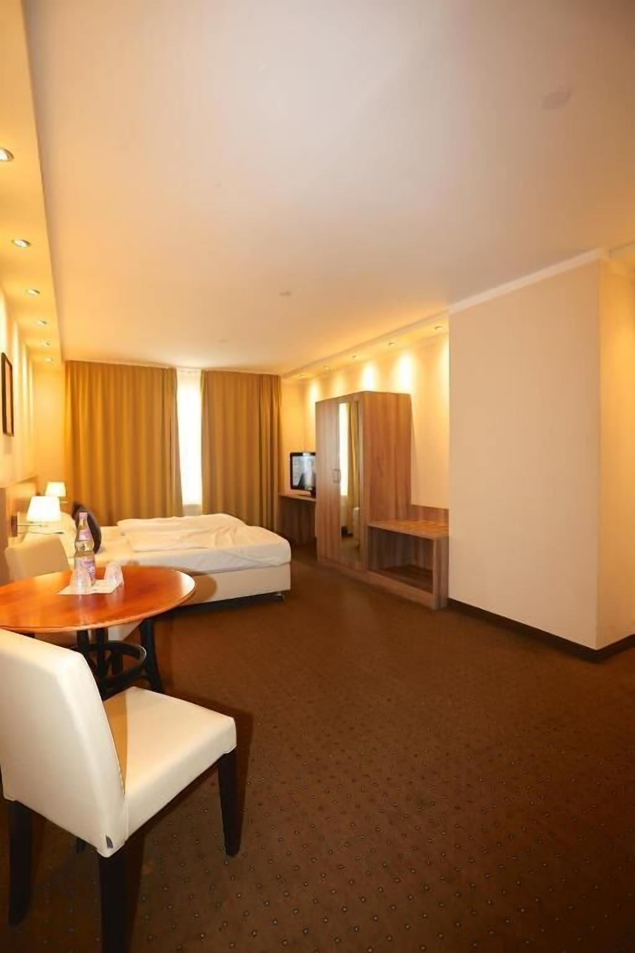 Habitación de hotel con cama, televisión, escritorio con silla y una mesita con una botella y vasos.