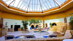 A spacious courtyard with a central fountain, stone walls, and a glass ceiling. - Carea Harz Hotel Allrode (Thale)