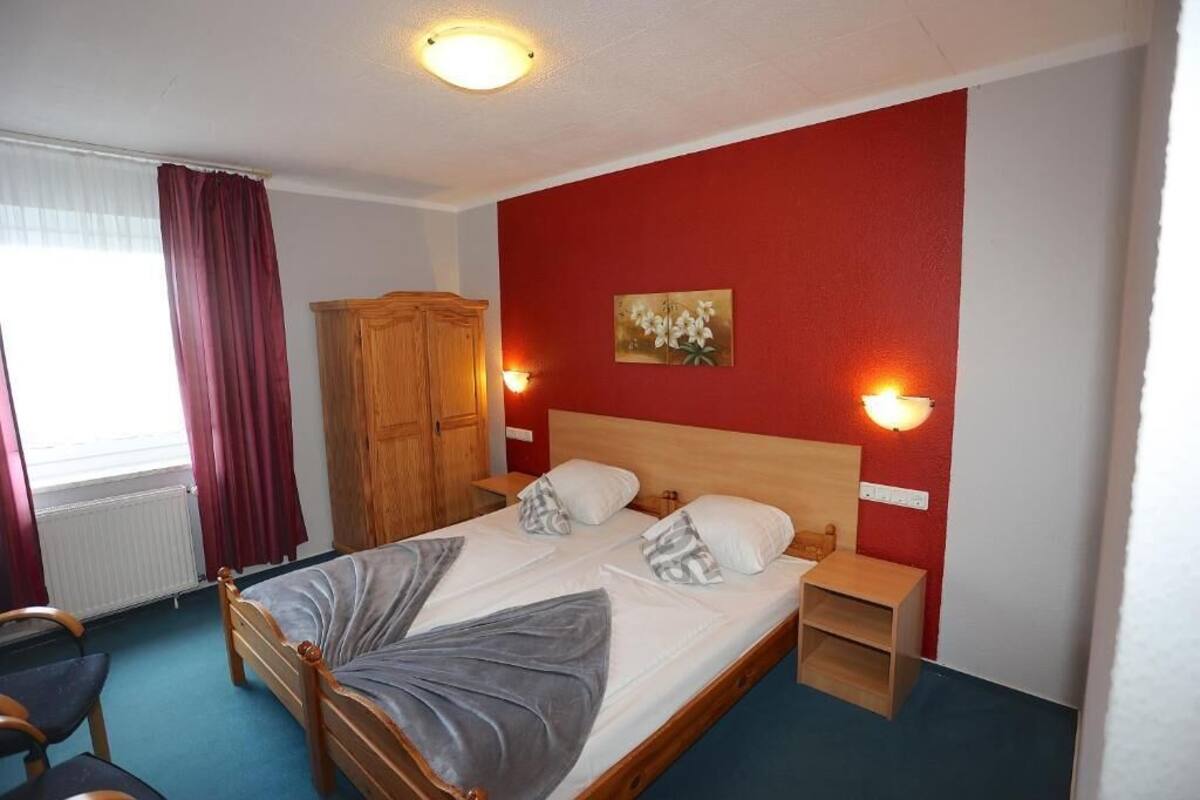 A single-bed room with a wooden headboard, two bedside tables, a wardrobe, and a window with curtains.