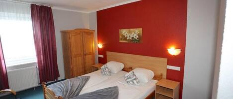 A single-bed room with a wooden headboard, two bedside tables, a wardrobe, and a window with curtains.