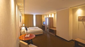 A hotel room with a bed, a desk, a chair, a small table, a TV, and a mirror. - Carea Harz Hotel Allrode (Thale)