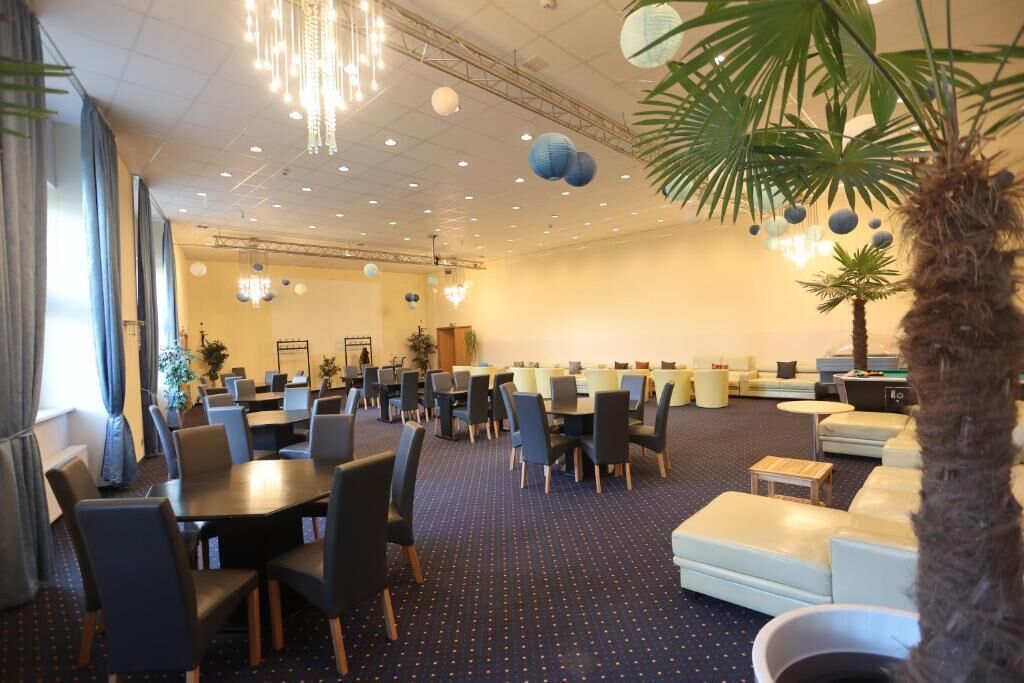 A spacious hotel lobby with multiple dining tables and chairs, a seating area with couches, and a large palm tree.