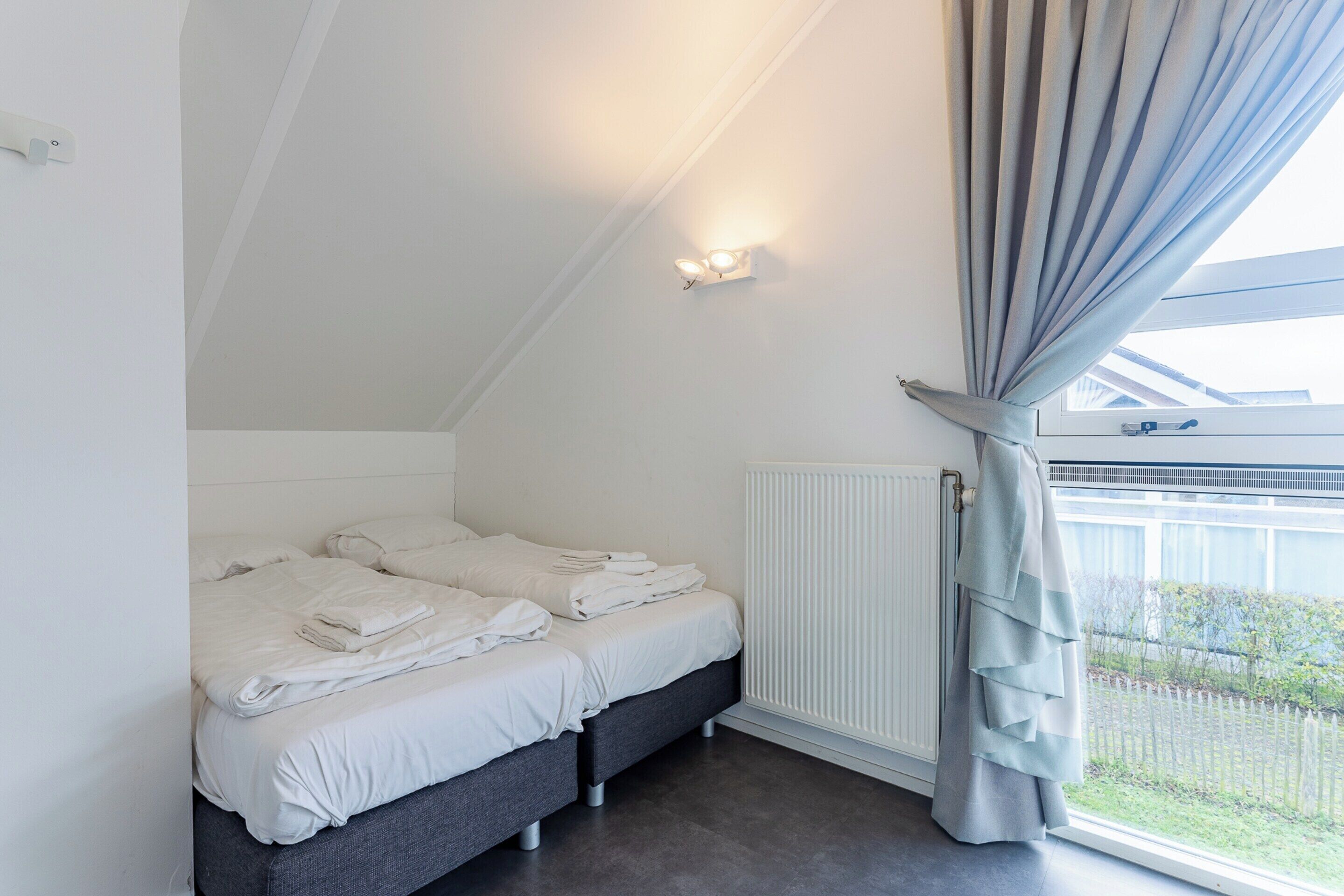 A bedroom with two beds, a window with curtains, a wall-mounted light, and a radiator.