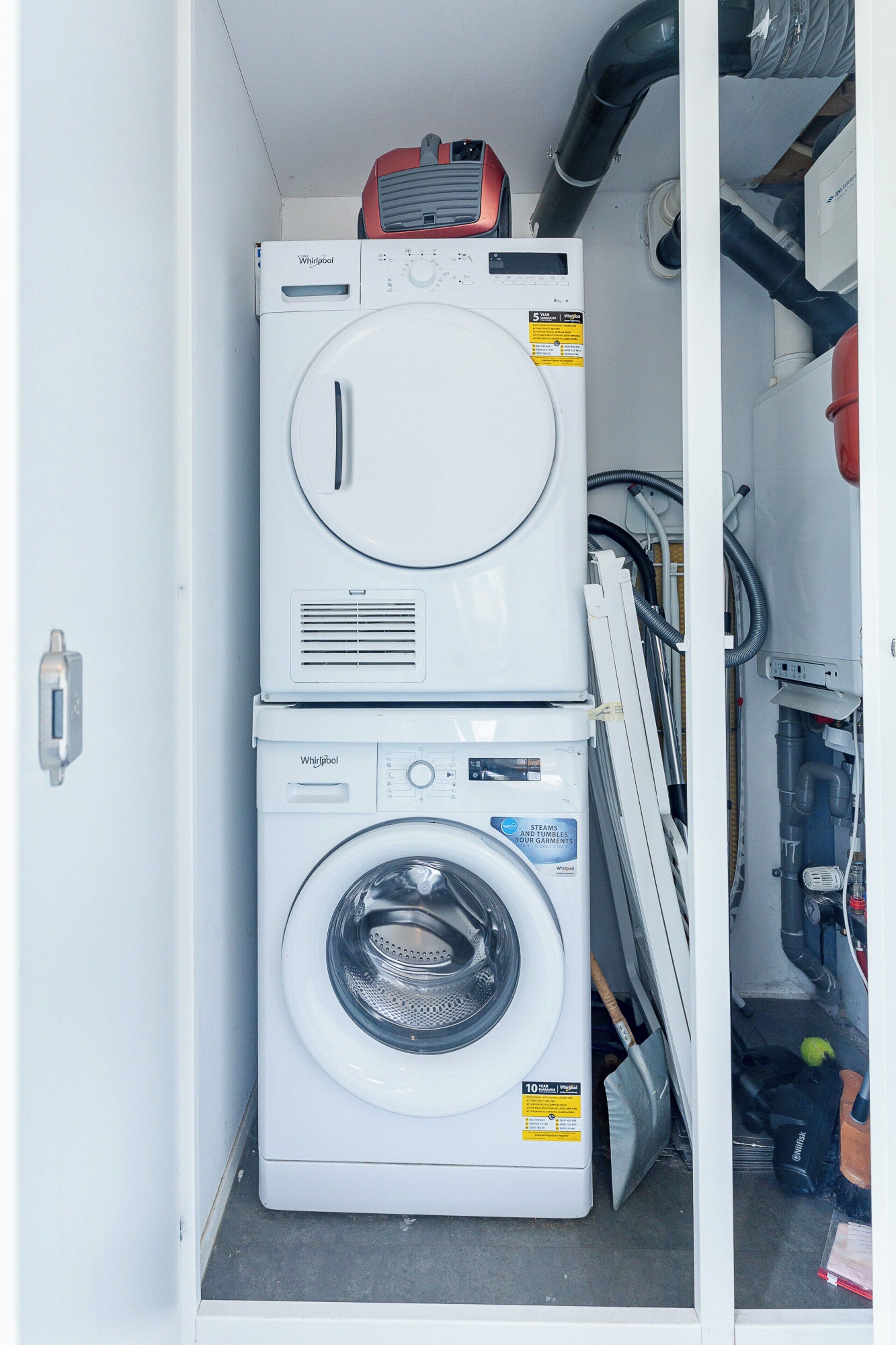 A compact laundry room with stacked appliances, including a washer and dryer, and visible plumbing and electrical connections.