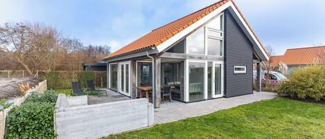 A modern house with a sloped roof, large glass windows, and a patio area.