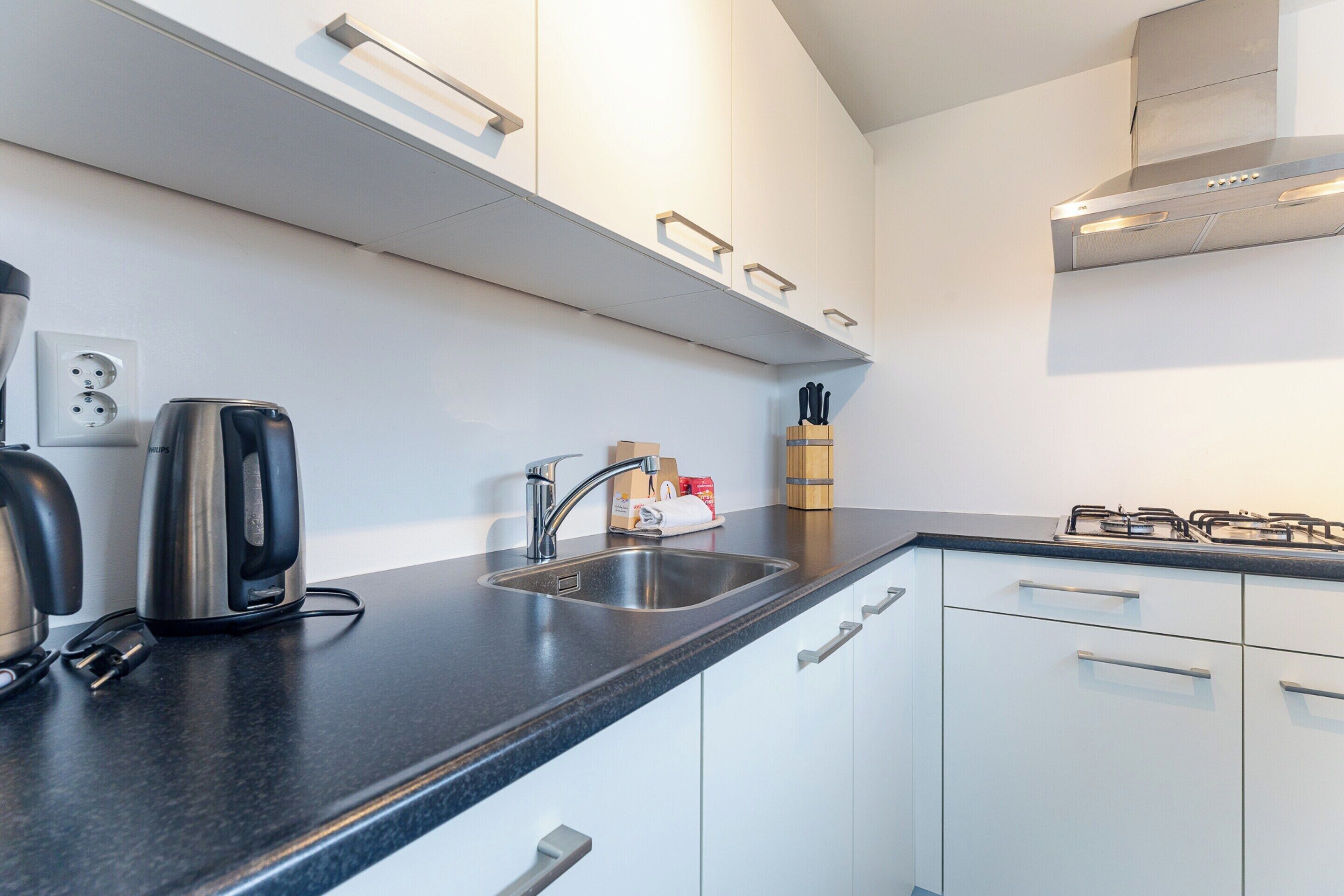 A modern kitchen with a stainless steel range hood, a built-in sink, and a black countertop.
