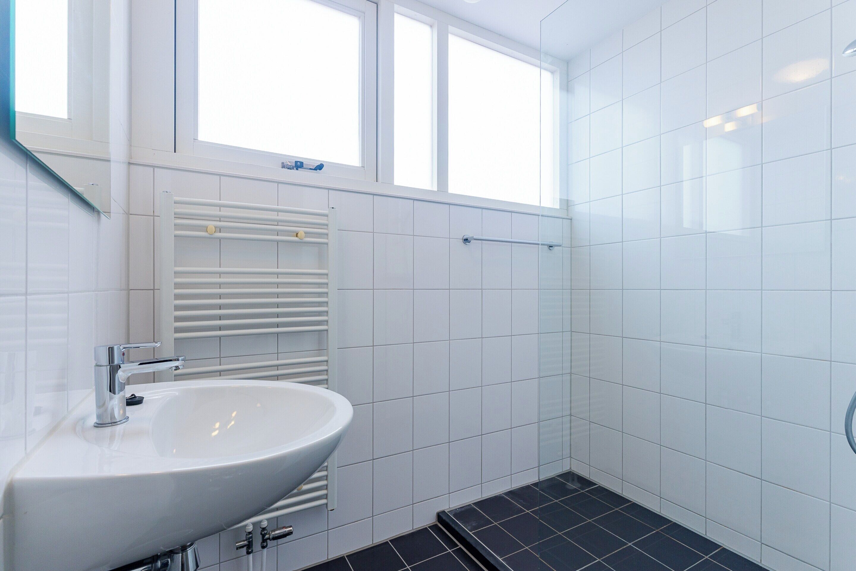 Un bagno con un lavandino bianco, uno specchio e una finestra sopra il lavandino.