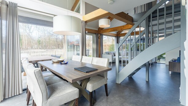 Un espace repas moderne avec une table et des chaises en bois, une grande fenêtre avec des rideaux et un escalier menant à un niveau supérieur.