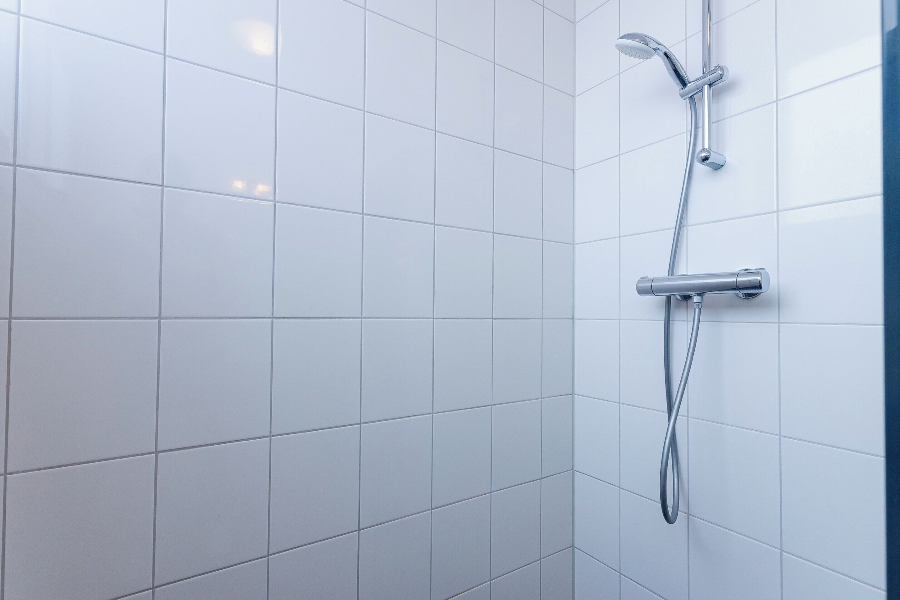 A modern bathroom with white tiles, a chrome showerhead, and a handheld shower attachment.