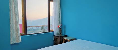 A bedroom with a bed, a window with curtains, a small table, and a nightstand.