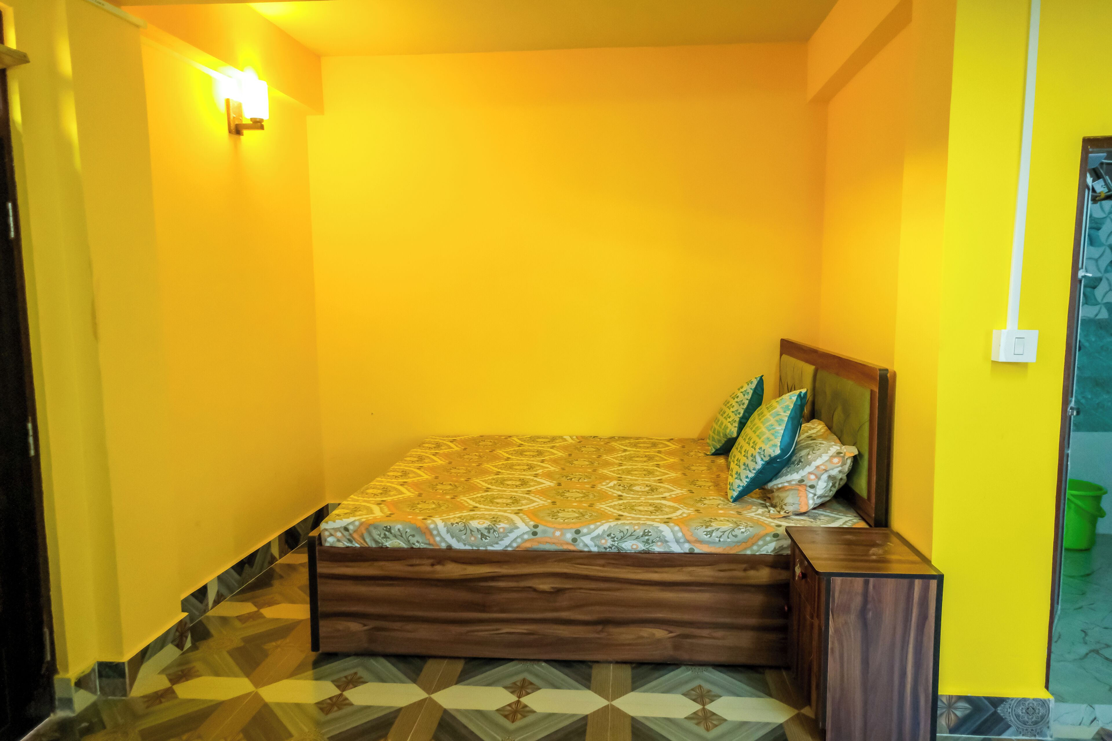Una habitación pequeña e iluminada con paredes amarillas, una colcha estampada y un diseño geométrico en el suelo.