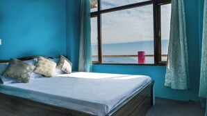A bedroom with a large window, a bed with white bedding, and a view of the mountains. - Mukhia Homestay (Kurseong)