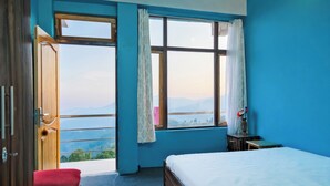 A bedroom with a large window, a bed, a red chair, and a small table. - Mukhia Homestay (Kurseong)