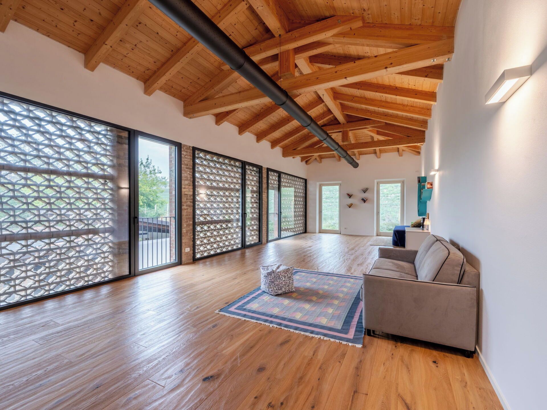 A spacious room with wooden flooring, a sofa, and a patterned rug.