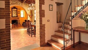 Eine Treppe mit Metallgeländer, die zu einer zweiten Etage führt, ein Kamin aus Ziegelsteinen und ein Essbereich mit Stühlen und Tisch.